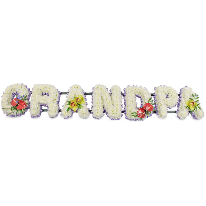 A striking funeral flower arrangement spells out "GRANDPA" in bold, capital letters, arranged in a long horizontal line and photographed against a simple, white background that brings every colour and texture into focus. Each individual letter is sculpted from densely packed white chrysanthemums, their tiny petals layered to form a thick, cushiony surface that looks soft to the touch and conveys a sense of purity and quiet respect. Around the base of the letters, a fine trim of pale lavender or soft purple ribbon encircles the design, just visible beneath the cloud of white blooms and adding a gentle halo of colour that frames the word without overpowering it. Dark green structural bars link the letters behind the flowers, giving the tribute stability so it can be displayed confidently at a church in New Barnet, a local cemetery, or during a farewell gathering near Oakleigh Park. Carefully placed accent sprays bring warmth and personality to the design: the letter 'G' and the letter 'D' are adorned with bold red anthuriums, their heart-shaped, glossy petals and golden spadices arranged among lush green foliage and a few dainty purple filler flowers. These focal points add depth, passion, and a feeling of heartfelt remembrance. The first 'A' and the final 'A' carry graceful clusters of yellow-green orchids, their elegant blooms and arching stems suggesting enduring love and precious memories. The overall effect is one of tenderness and strength, a bespoke grandfather tribute that speaks clearly of family ties and love shared over a lifetime, crafted with the sensitivity of a local New Barnet florist who understands the importance of saying goodbye beautifully.